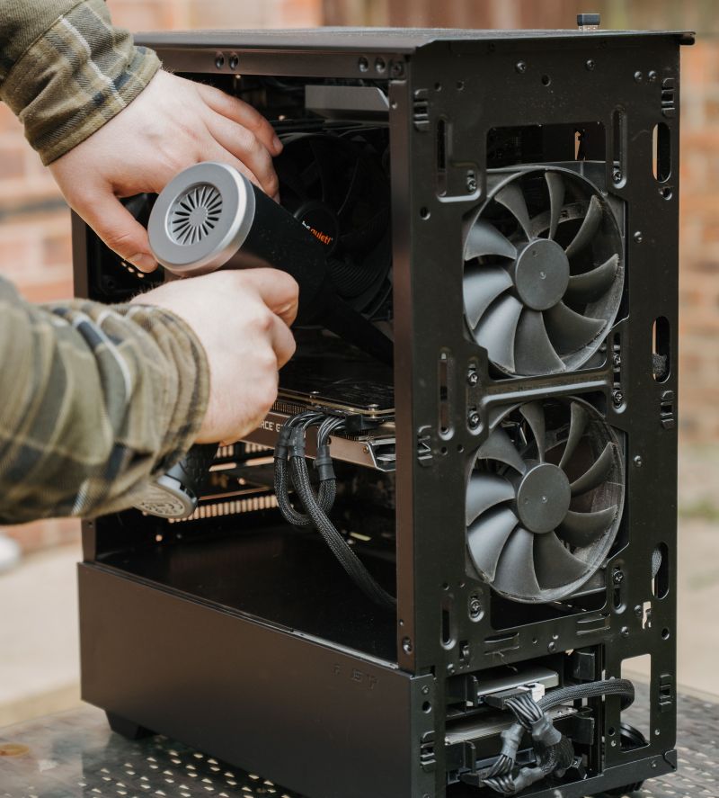 A technician using an electric duster to clear dust from the fans of an open desktop PC case to fix overheating.