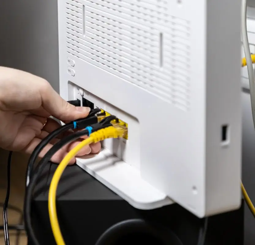 A technician plugging yellow ethernet cables into a white Wi-Fi router to configure a home network at New Ross PC Repairs.