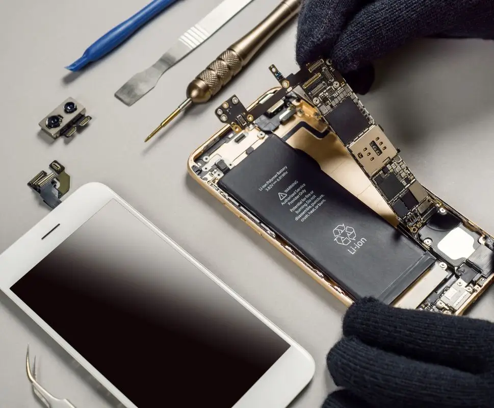 A technician carefully disassembling a broken smartphone to repair the logic board and battery at New Ross PC Repairs.